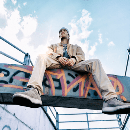 A man on a concrete beam in a subway with graffiti in the background