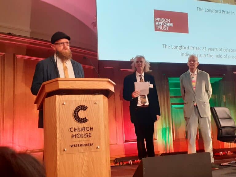Brendan Ross stood at a lectern giving a speech after winning his award. Wearing shirt, tie and blazer.