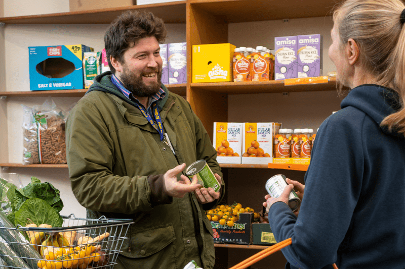 Photograph of Man explaining to a customer how the Pantry works, infront of shelves full of healthy produce.