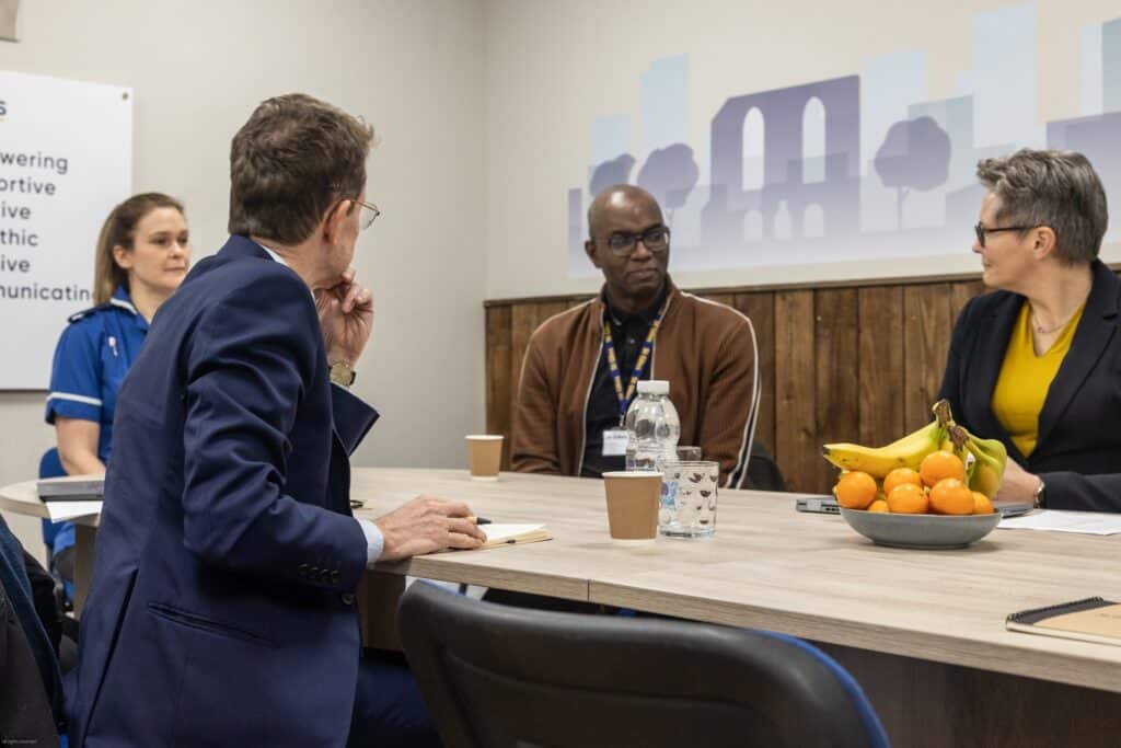 Photograph of Andy Street and Tracey Burley sat around a table talking with St Giles staff in St Giles Midlands office