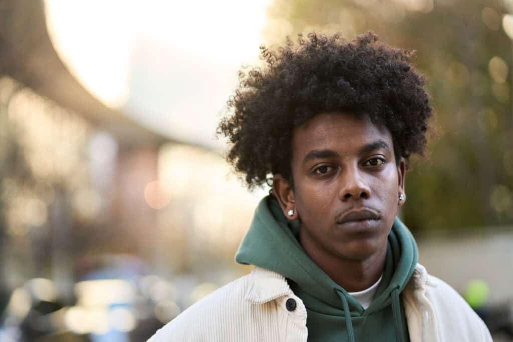 Photograph of Paul* stood outside on a sunny day wearing a hoodie and light brown jacket.