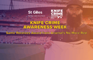Photograph of Samir in front of the Arsenal FC crowd holding a all white football shirt. Text "Knife Crime Awareness Week: Samir Receives Award from Arsenal's No More Red"
