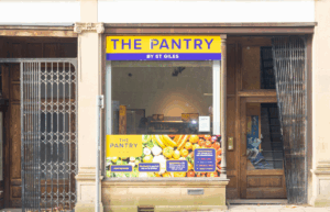 Photograph of open and welcoming St Giles Pantry entrance with closed down shops and barrier either side.