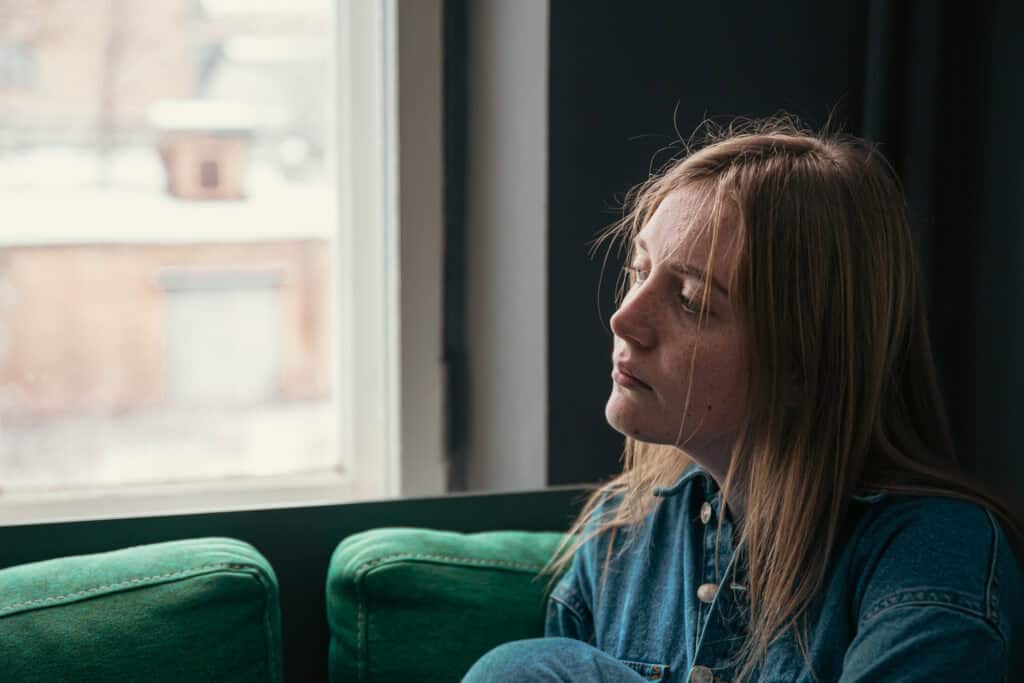 A beautiful young woman is sitting on the sofa by the window on a cold winter day.