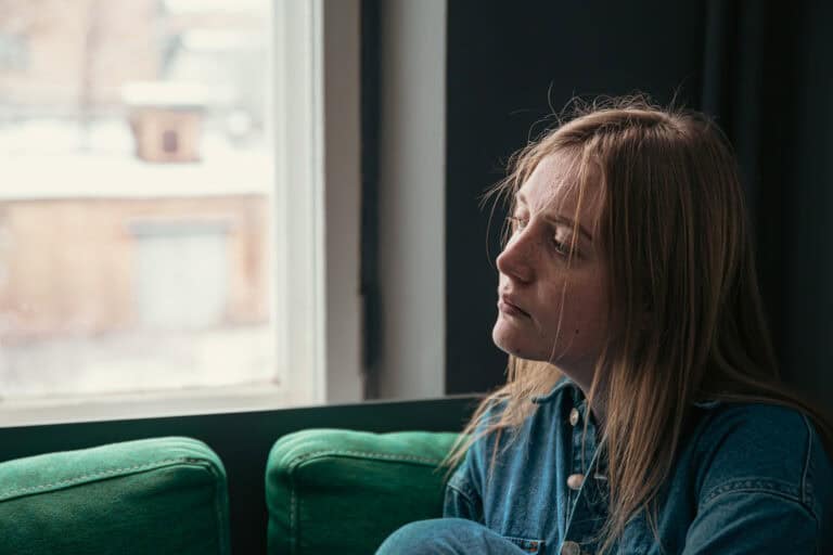 A beautiful young woman is sitting on the sofa by the window on a cold winter day.