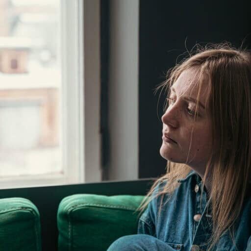 A beautiful young woman is sitting on the sofa by the window on a cold winter day.
