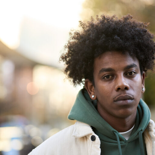 Photograph of Paul* stood outside on a sunny day wearing a hoodie and light brown jacket.